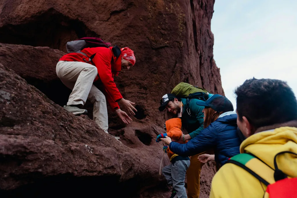 Group of hikers helping each other climb a rocky mountain outdoors.